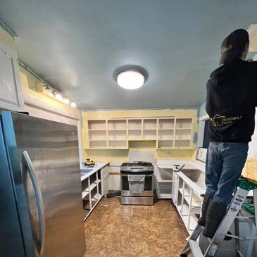 Person standing on ladder renovating kitchen cabinets and walls.