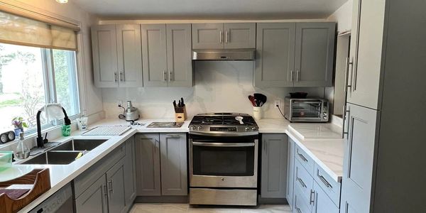 Modern kitchen with gray cabinets, stainless steel stove, and white countertops.