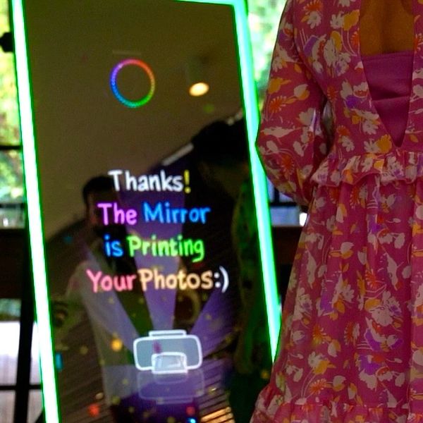 A mirror with colorful text printing photos for a person in a floral dress.
