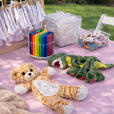 Colorful markers, craft supplies, and plush toys on a pink table outdoors.