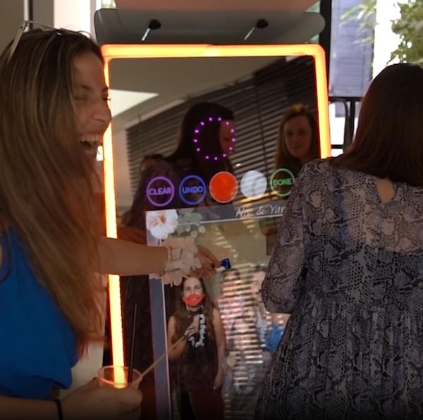 Two women enjoying and interacting with a digital photo booth mirror.