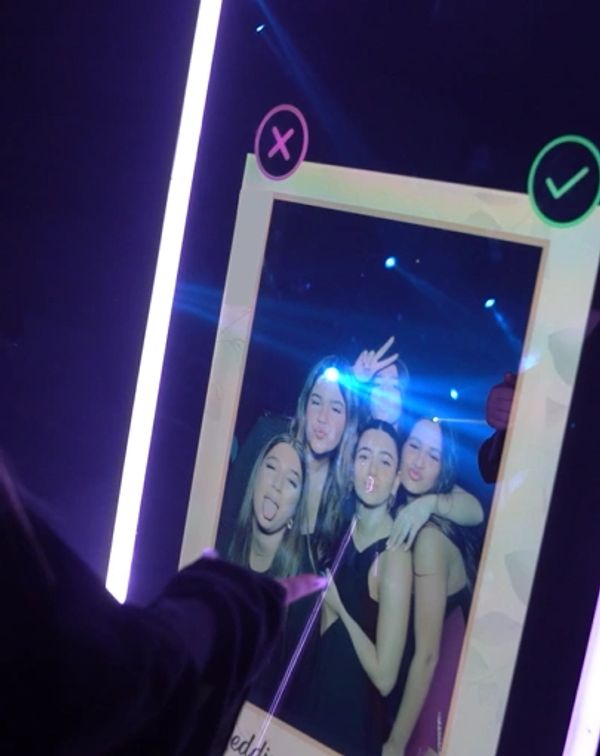 Friends posing playfully in a photo booth with neon lights.