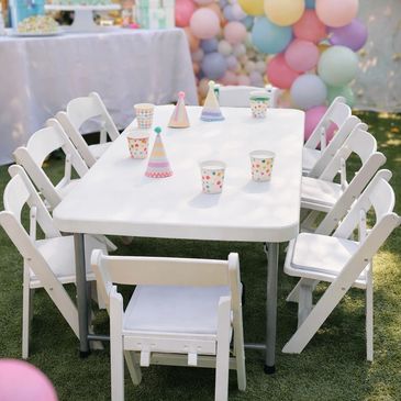 White table with chairs and party hats at an outdoor celebration.