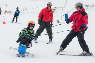 Skier sitting in a bi-ski tethered by an instructor. 
