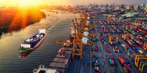 A busy container port at sunset with ships and cranes along the river.