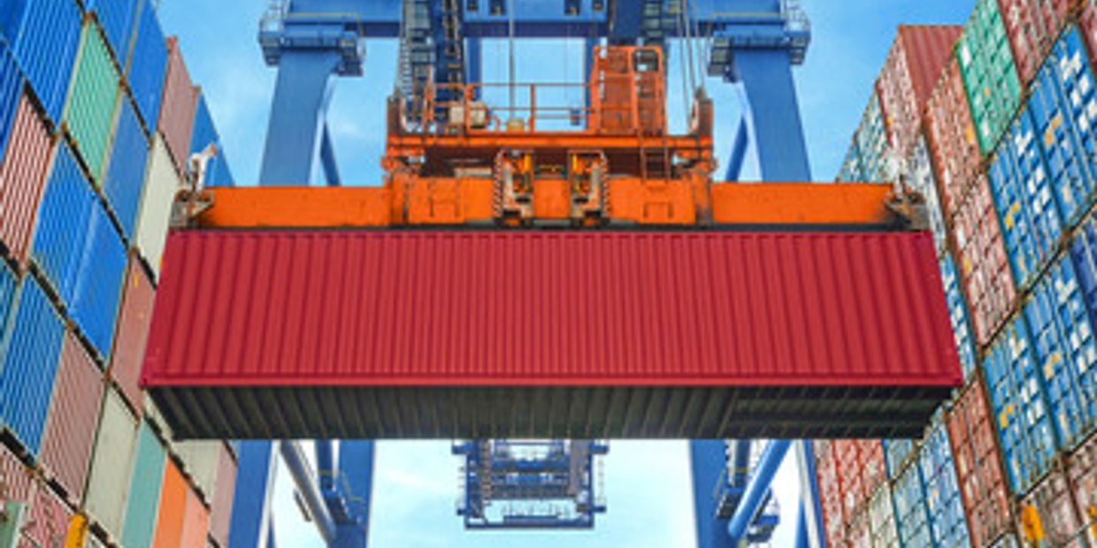 A red shipping container being lifted by a crane at a busy port.