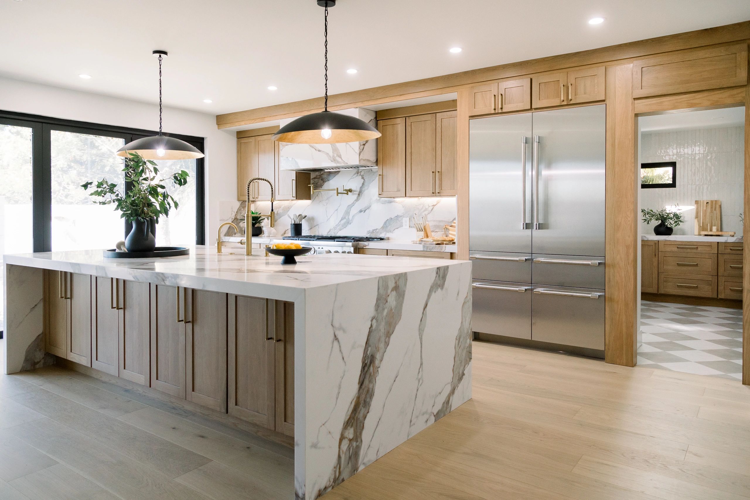Wide shot, left view of kitchen. Two black hanging lights above the kitchen island.  
