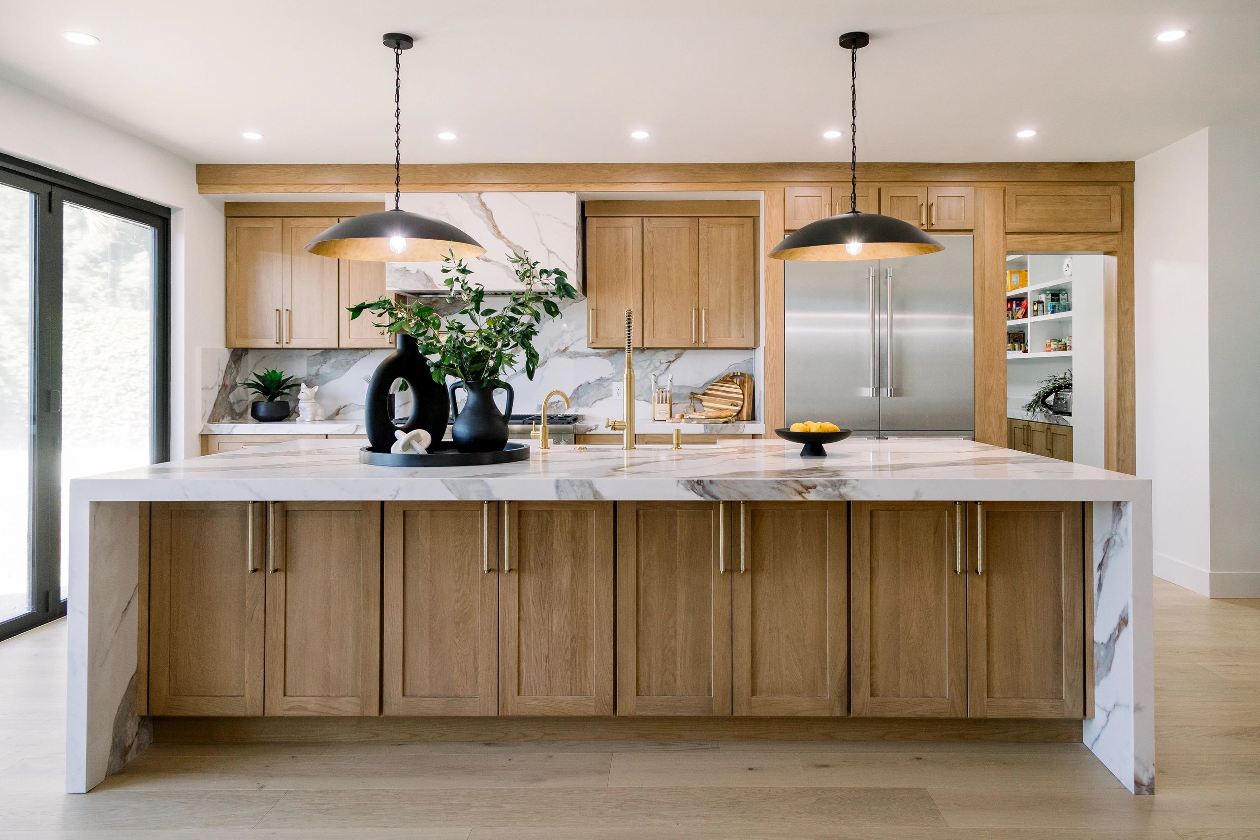Wide angle of kitchen island with white quartz countertop and light brown wooden cabinets below. 