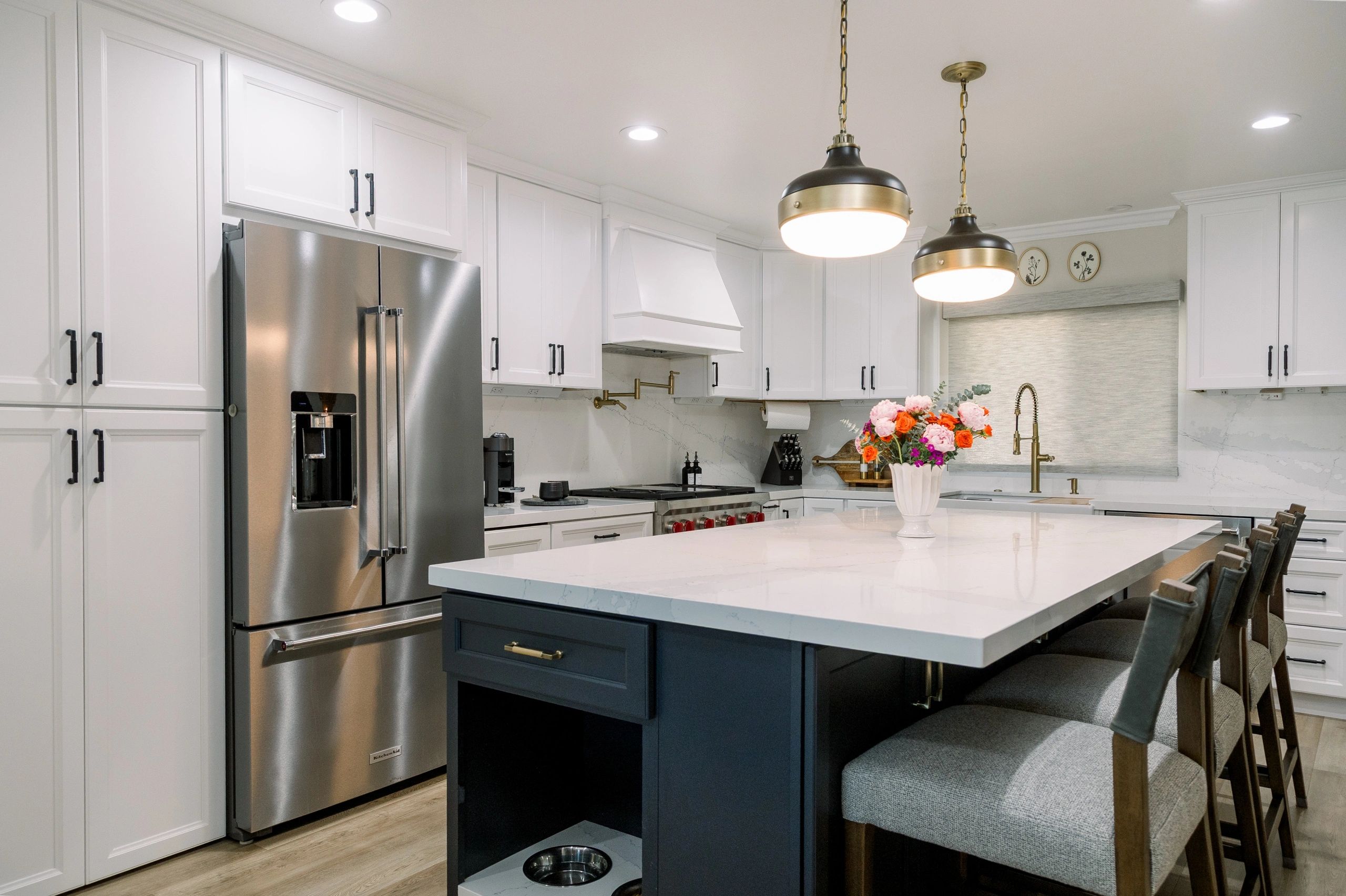 Side view of kitchen with stainless steel fridge, white island counter top, and seating area. 