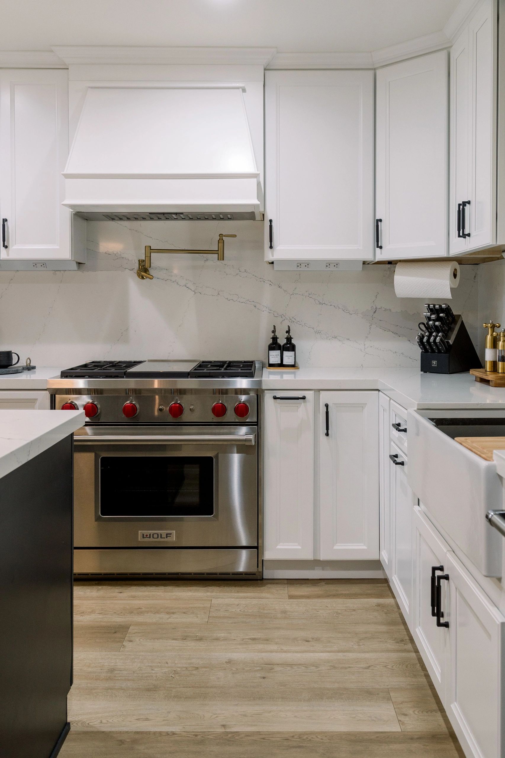 Direct view of the stainless steel stove with red knobs. White cabinetry with black handles. 