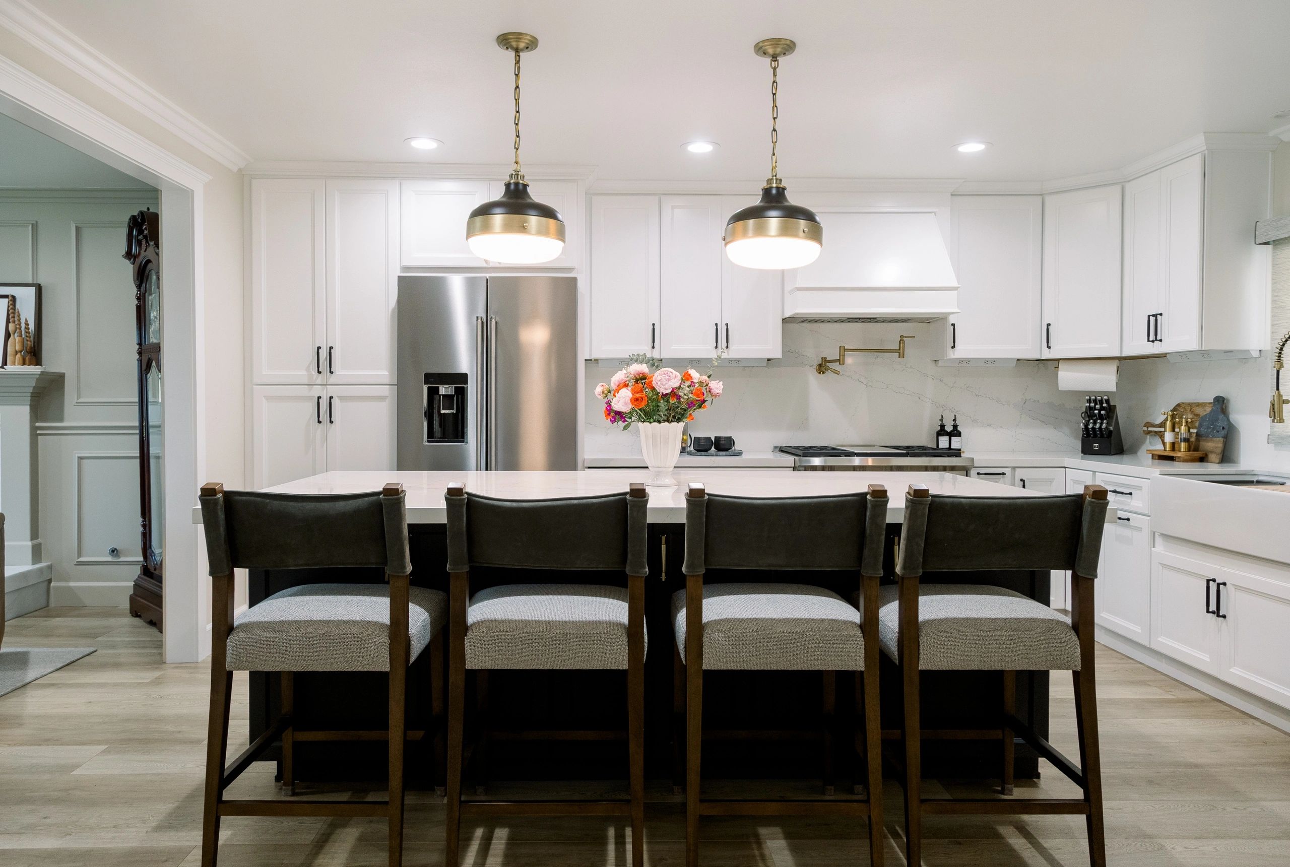 Wide view of island seating area with color flowers on counter top with two hanging lights above. 