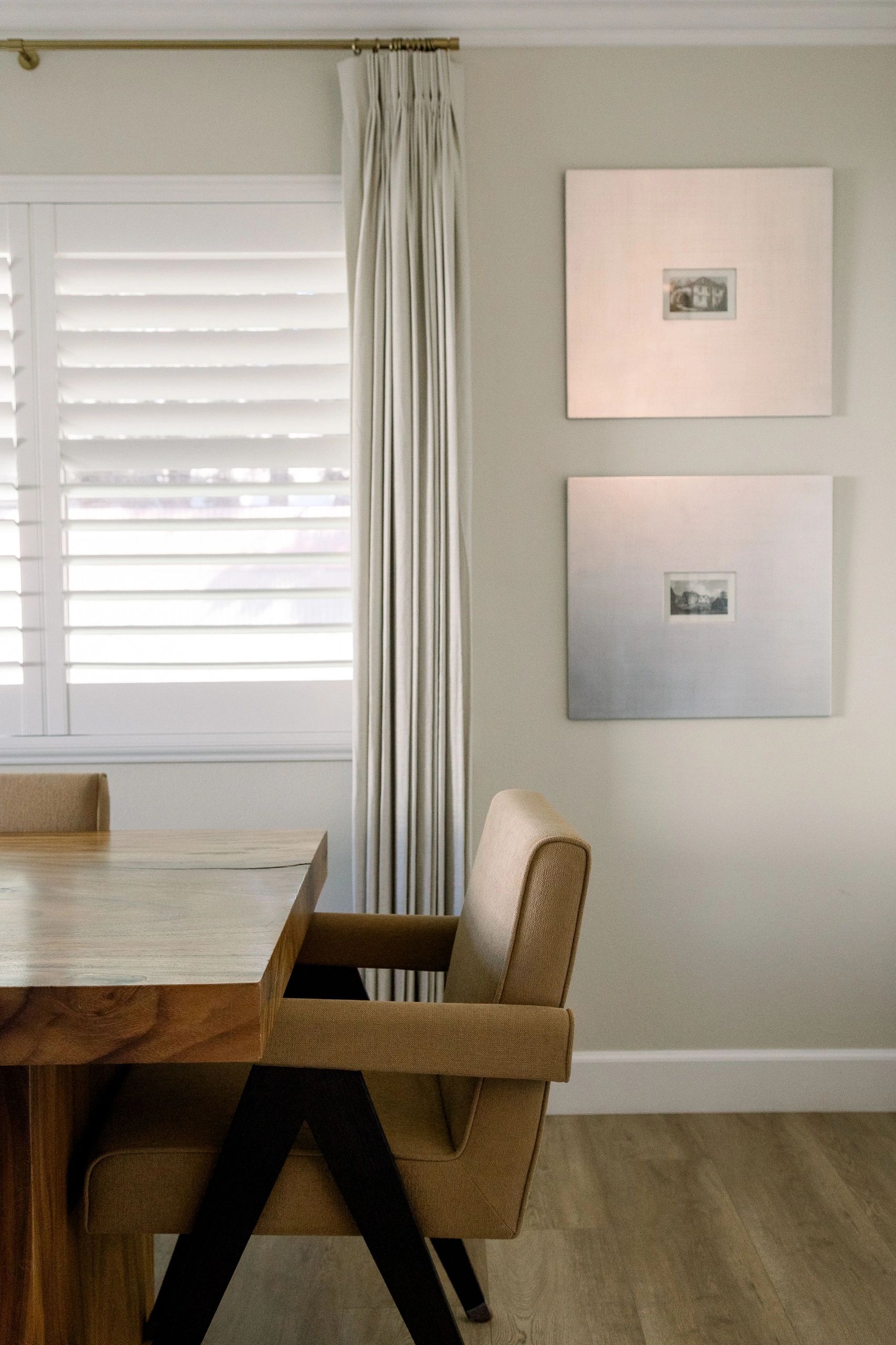 Partial view of dining table near a window with open blinds; framed artwork hangs on the wall behind