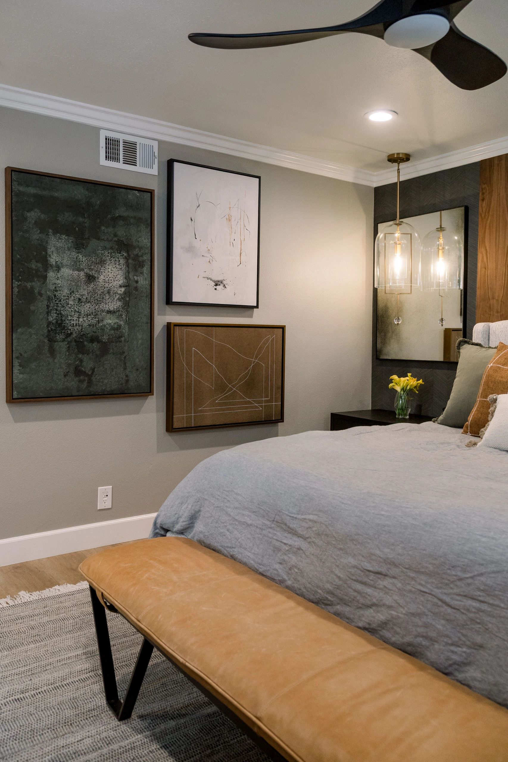 Side view of a bed with grey bedding; green, white, and brown framed artwork hangs on adjacent wall.