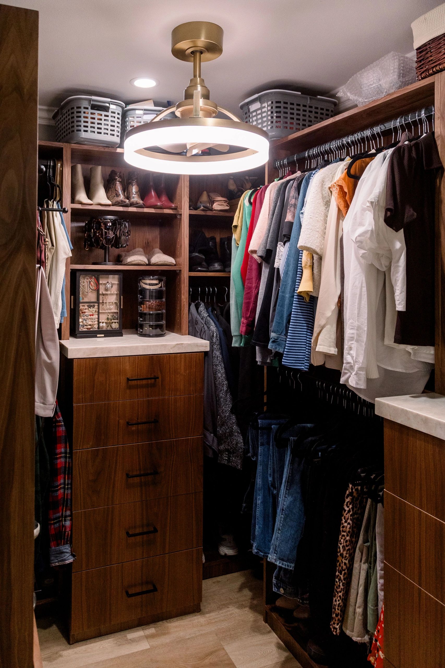 Custom closet with brown wooden cabinetry, hanging clothes, and organized shoes and jewelry.