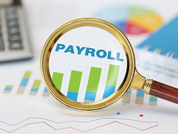 Magnifying glass highlighting payroll bar chart on financial documents.