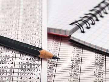 Close-up of a pencil on financial data sheets with a spiral notebook.