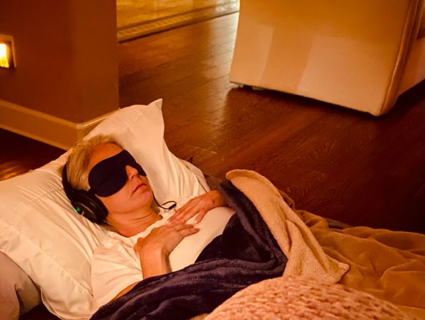 Person resting with an eye mask and headphones under warm blankets.