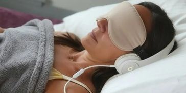 Woman sleeping with eye mask and headphones under a blanket.