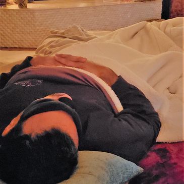 Person resting on a couch covered with a blanket, eyes closed.