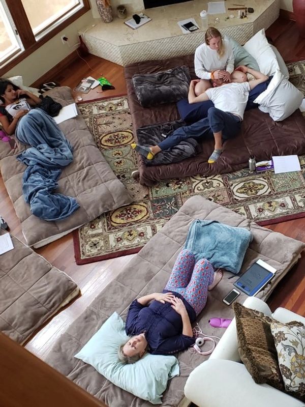 Four people relaxing on mattresses in a cozy living room with blankets and pillows.