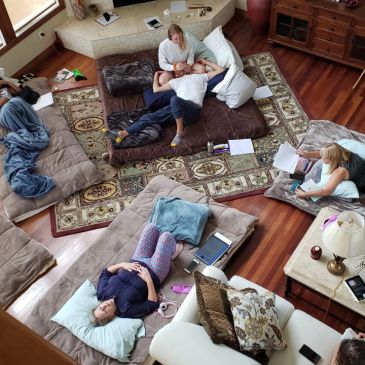 People relaxing on cushions and sofas in a cozy living room with wooden floors.