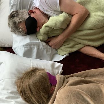 Two people lying in bed, one wearing an eye mask.