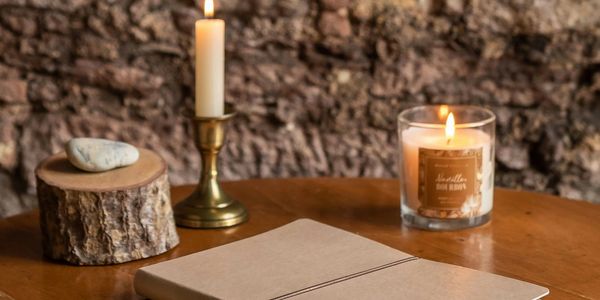 Cozy writing setup with candles and a notebook on a wooden table.