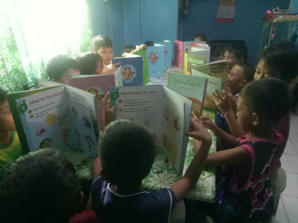 Children sitting around a table, reading colorful books together.