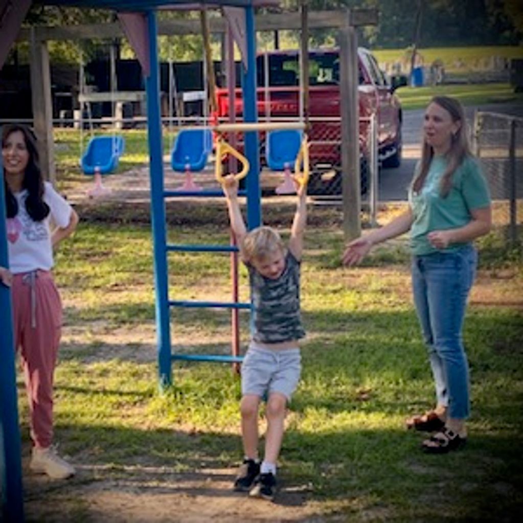 Child playing on monkey bars with two women watching.