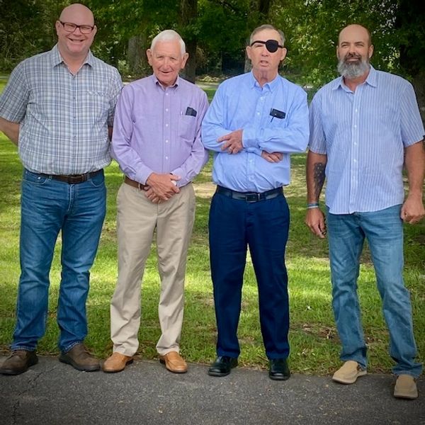 Four men posing together outdoors on a pathway.