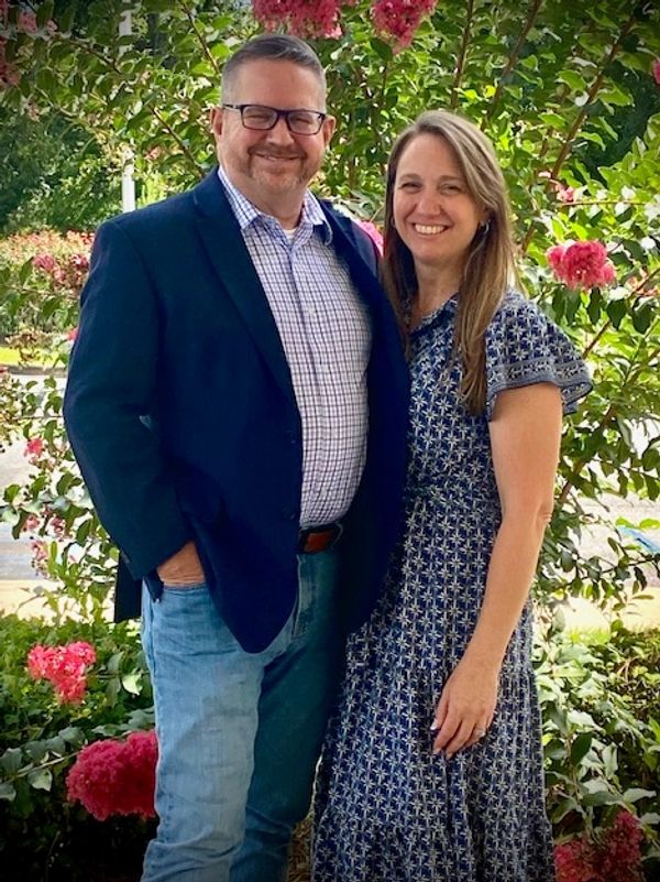 Smiling couple posing outdoors among blossoming flowers.