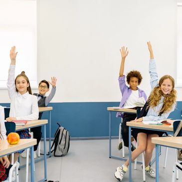 Four enthusiastic students raising their hands in a bright classroom.