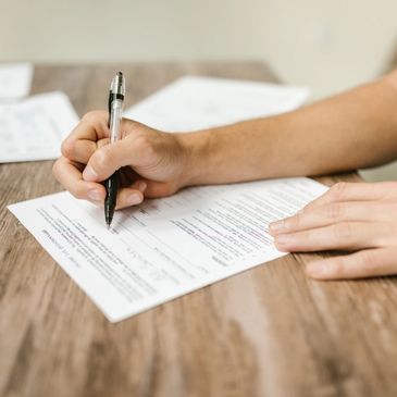 Person filling out a form with a pen on a wooden table.