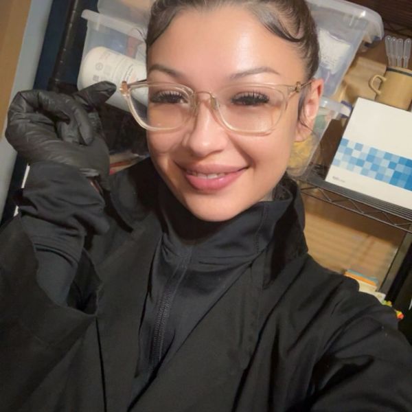 Woman wearing glasses and black gloves smiling indoors.