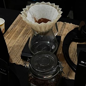 Coffee brewing setup with ground coffee in filter and beans in jar.