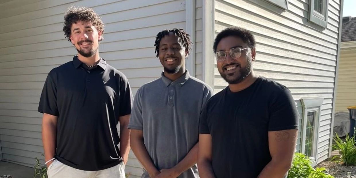 Three men standing together outside a house on a sunny day.