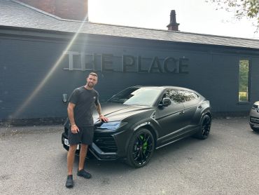 Man posing next to a black luxury SUV in front of a building.