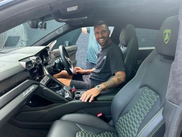 A man smiles inside a Lamborghini car, showing the luxurious interior.
