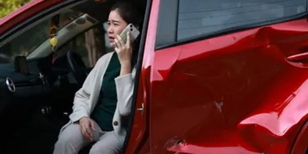Woman talking on phone beside a damaged red car.
