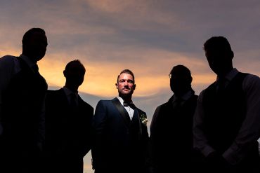 Groom posing with groomsmen at sunset.