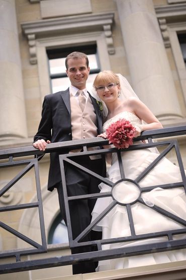 Happy couple in wedding attire posing on balcony.