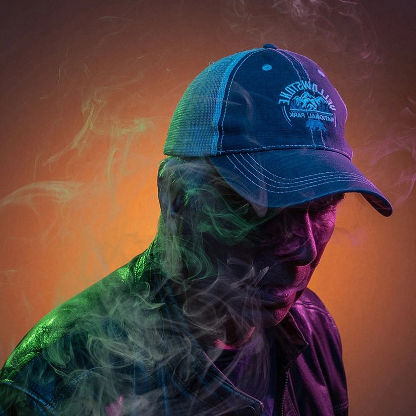 Man wearing a cap and leather jacket surrounded by colorful smoke.