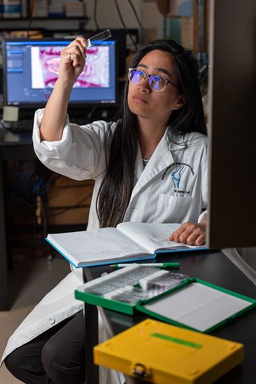 A scientist examining a microscope slide in a lab while referencing a book.