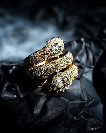Three glittering gold diamond rings on a dark textured surface.