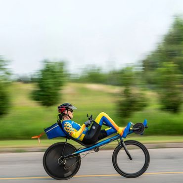 A cyclist in a blue and yellow suit rides a recumbent bike on a road.