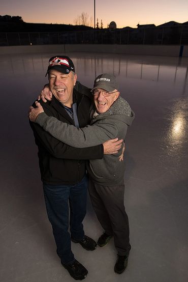 Two elderly men sharing a joyful hug on an ice rink at sunset.