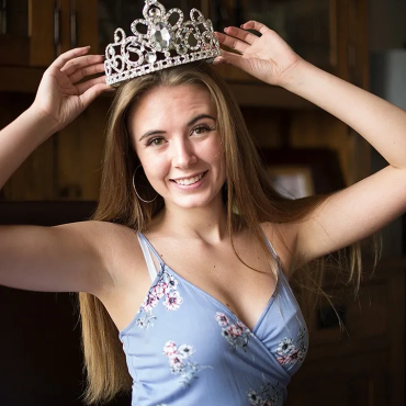 Young woman smiling while placing a jeweled crown on her head.