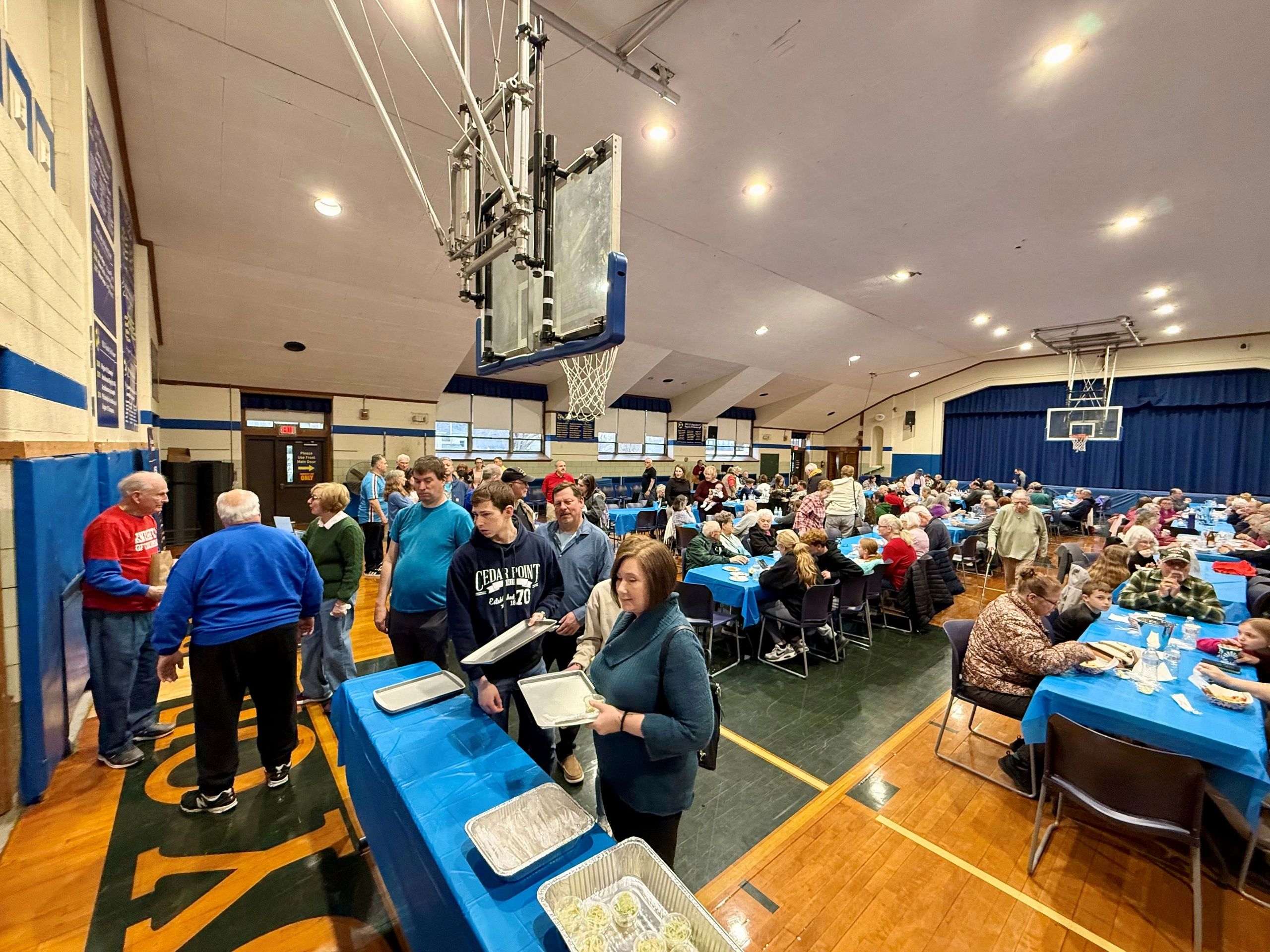Community gathering in a gymnasium with people lining up for food.