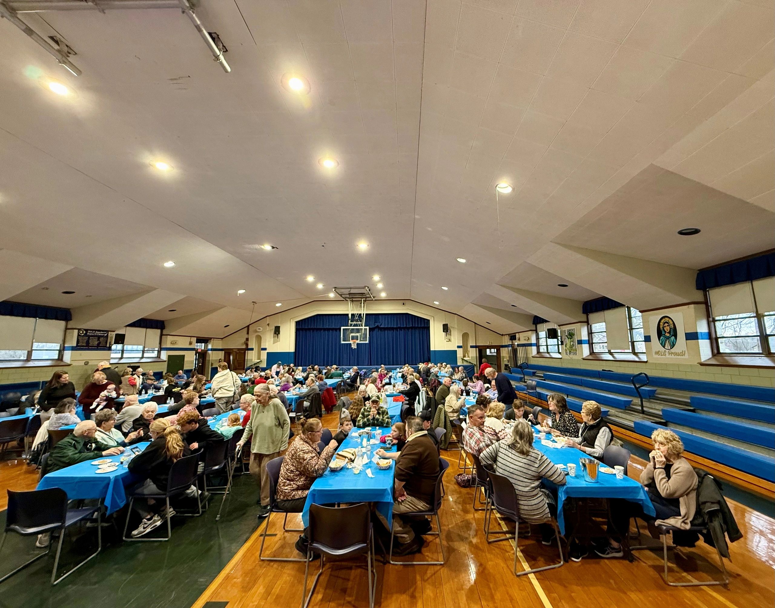 Community gathering in a gymnasium with tables and people eating.