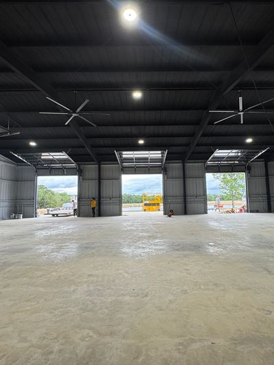 Inside view of a large empty warehouse with open garage doors and ceiling fans.